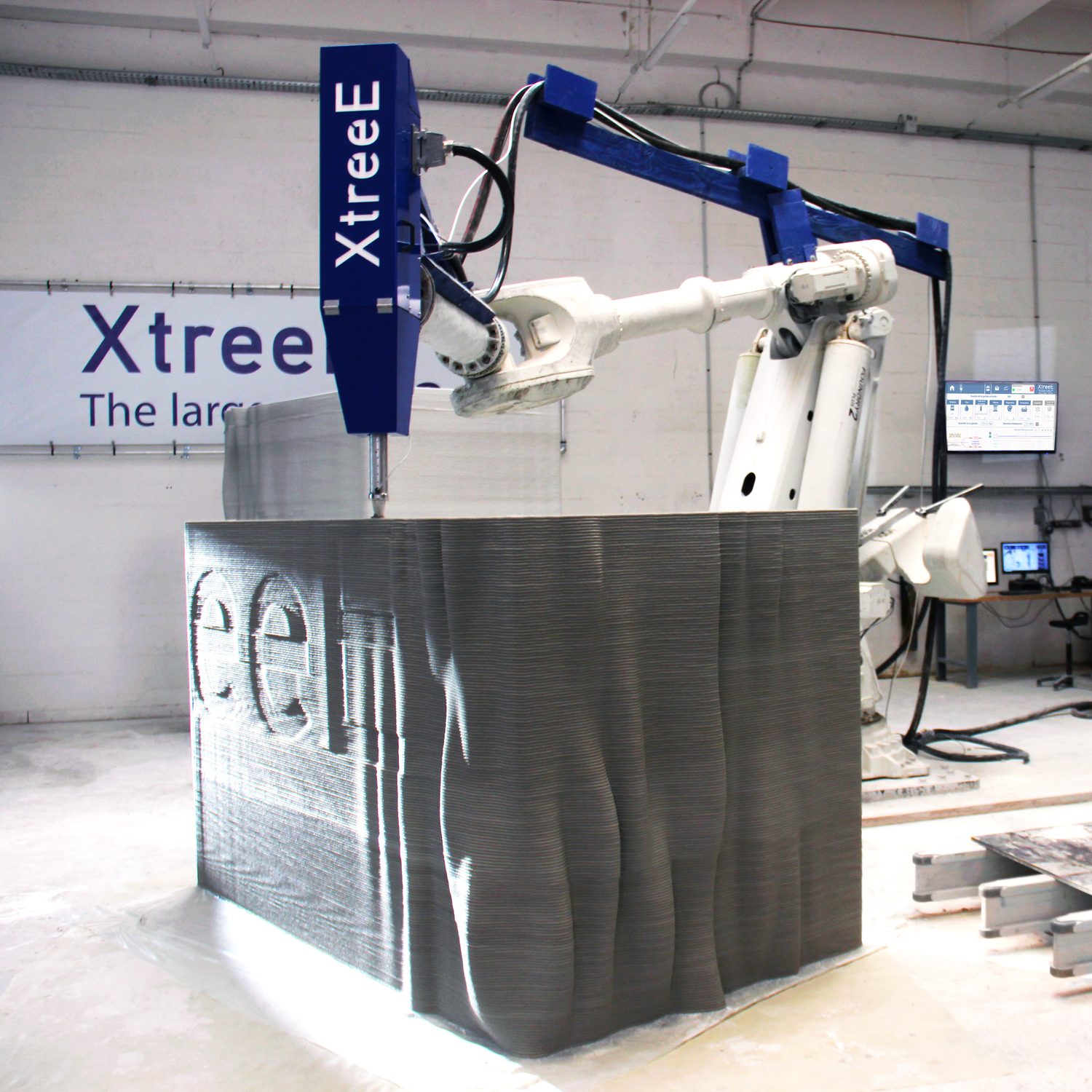 Cellule robotisée XtreeE imprimant un mur en béton dans l'atelier
